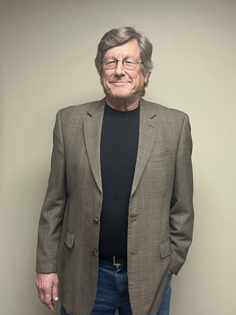 A man in a suit and glasses standing with his hands in his pockets.